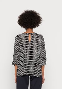 Blouse à motifs noirs et blancs avec manches trois-quarts, coupe ample et ouverture en forme de goutte d'eau dans le dos. Texture de tissu lisse.