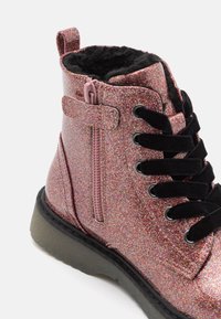 Stivaletto rosa glitter con lacci neri, tessuto testurizzato e chiusura laterale con zip. Suola in gomma con tacco leggero.