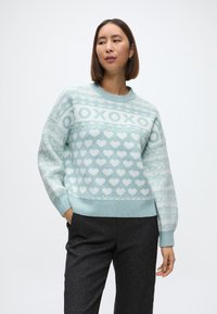 Gaiši zils adīts džemperis ar sirds rakstiem, apaļu kakla izgriezumu, ribotām piedurknēm un apakšmalu, nedaudz pārlieli piedurknes un mīkstu tekstūru.