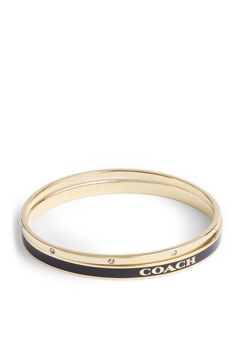 Guldtonad metallarmband med svart emaljinlägg, präglad "COACH"-logotyp och små klara stenar längs kanten.