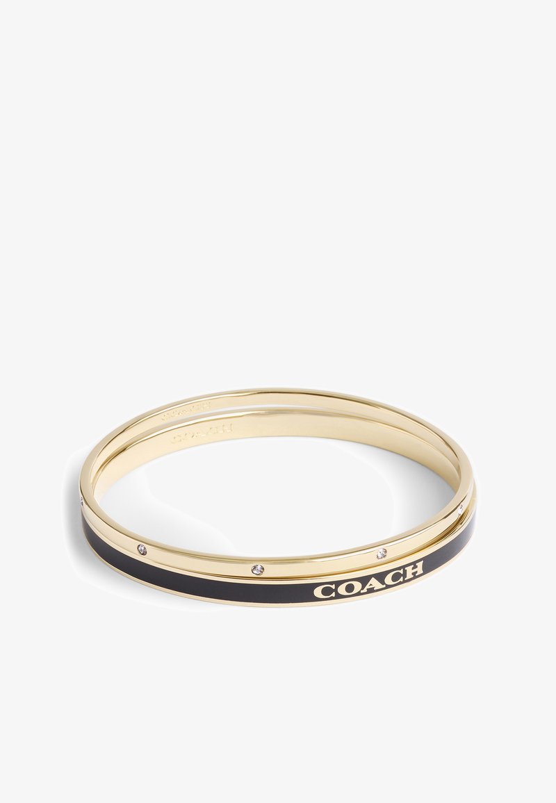 Guldtonad metallarmband med svart emaljinlägg, präglad "COACH"-logotyp och små klara stenar längs kanten.