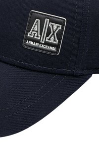 Cappello blu navy con un patch nero con il testo bianco "A/X" e "Armani Exchange". Realizzato in tessuto testurizzato con cuciture visibili.