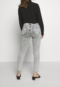 Jeans gris de cintura alta y ajustados, con un acabado desgastado, que cuentan con dos bolsillos traseros y detalles de costura, combinados con una blusa negra de manga larga.