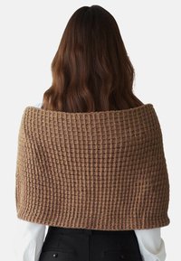 Shawl marrone texturizzato con un motivo a maglia waffle, che cade sulle spalle. Realizzato in un materiale morbido, presenta una vestibilità ampia e comoda.