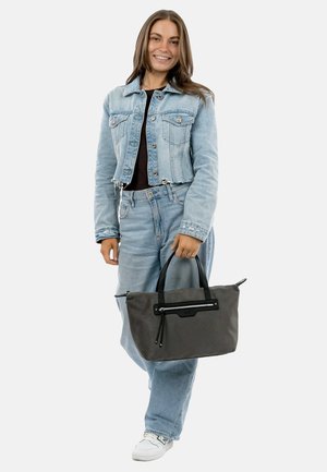 Gray tote bag with black accents, rectangular shape, zipper closure, and dual handles. Worn with a denim outfit and white sneakers.