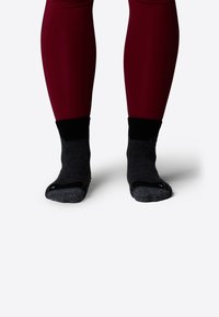 Czarno-szare skarpetki ankle z teksturowanym wzorem, kontrastującym czarnym mankietem, noszone z dopasowanymi czerwonymi legginsami. Skupienie na stopach i wzorze skarpetek.