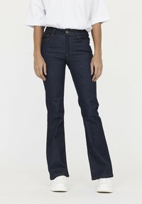 Donkerblauwe uitlopende jeans met een vijf-pocket ontwerp, sluiting aan de voorkant met een knoop, en contrasterend stikken. De stof heeft een gladde denimtextuur.