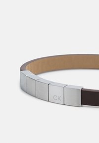 Brown leather belt featuring metallic silver hardware with a block design and engraved "CK" detail on one of the metallic sections.