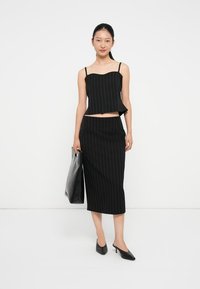 Top corto de rayas negras con tirantes finos, combinado con una falda lápiz a juego. La modelo sostiene un bolso tote negro y lleva puestos unos tacones negros de punta.