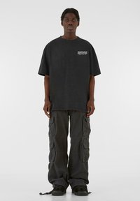 Storskala sort bomulds t-shirt med frontgrafik, kombineret med løse sorte cargo-bukser med flere lommer og snoretrækskanter.