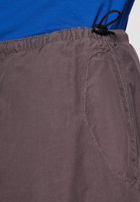 Shorts gris avec taille élastique, cordon de serrage et poches latérales. Texture lisse, matériau léger.