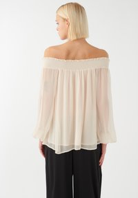 Off-the-shoulder kreminė bluzonė, pagaminta iš permatomo audinio, su smulkinta apykakle, ilgomis plačiomis rankovėmis ir laisvu siluetu.