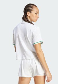 Top corto blanco con patrón de diamantes texturizado, mangas cortas a rayas verdes, combinado con pantalones cortos blancos, mostrando un material ligero.