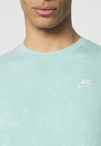 Mátově zelené tričko vyrobené z měkké bavlny, s kulatým výstřihem a malým bílým vyšitým logem Nike na levé straně hrudi.