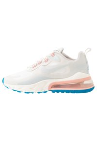 Bílé a světle šedé tenisky s růžovými akcenty, modrou podrážkou a viditelným vzduchovým polštářem v patě, zobrazené z boku na bílém pozadí.