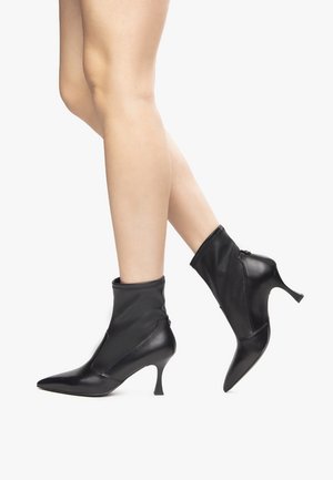 Sorte ankelstøvler med spids tå, lavet af læder, med en strækbar overdel, slank hæl og en lynlåsdetalje bagpå.