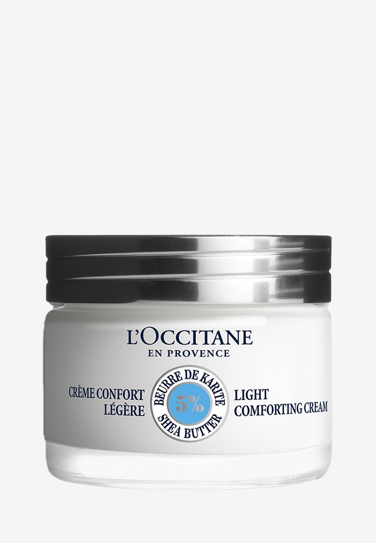 L'Occitane Light Comforting Cream i et klart glas krus med et sølvmetal låg. Har blå tekst og en cirkulær etiket med 5% sheabutter.