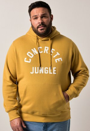 Felpa gialla con cappuccio che presenta la scritta "CONCRETE JUNGLE" in lettere bianche, con tasca frontale e polsini a costine. Il tessuto sembra morbido.