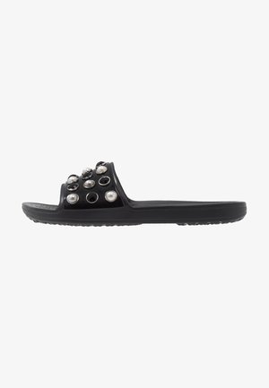Sandale à glissière noire avec une tige brillante ornée d'accents décoratifs ronds noirs et perle, semelle plate avec une prise texturée.