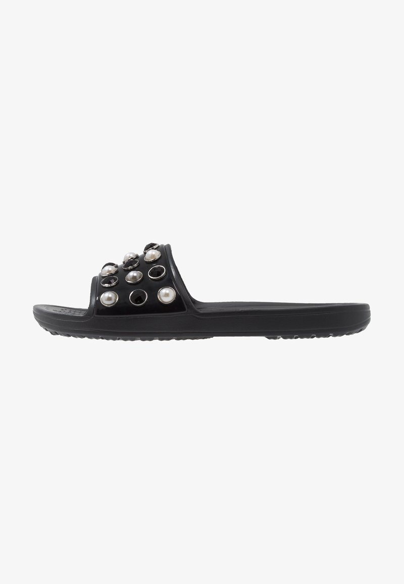 Sandale à glissière noire avec une tige brillante ornée d'accents décoratifs ronds noirs et perle, semelle plate avec une prise texturée.
