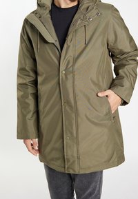 Oliven grøn, vandtæt parka med hætte, frontlukning med trykknapper og sidelommer. Glat tekstur, funktionelt design og synlig syning.