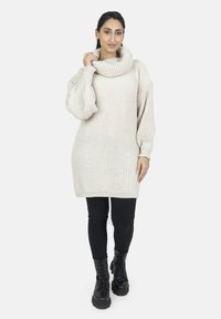 Krämfärgad oversized stickad tröja med hög hals, ribbat mönster och långa, voluminösa ärmar. Matchas med svarta leggings och kängor.