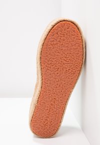 Natural fiber sole with a textured orange rubber base, featuring a rounded edge and layered jute-like material along the sides.