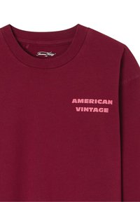 Sweatshirt bordeaux avec un col rond et un petit logo rose "AMERICAN VINTAGE" imprimé sur le côté gauche de la poitrine. Texture de tissu douce.