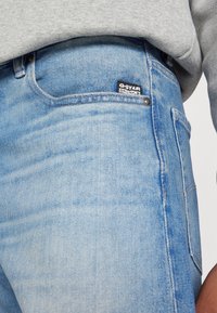 Lys blå denimjeans med en falmet finish. Har en sort G-Star Originals-lap på frontlommen og metalhardware-detaljer.