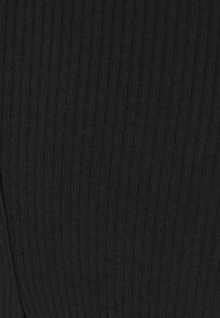 Czarna prążkowana tkanina o teksturowej powierzchni, z pionowymi liniami i miękką, elastyczną jakością, odpowiednia do projektowania odzieży.