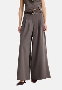 Bruine wijde broek met een geplooid ontwerp, met een aansluitende tailleband en een bruine riem met een gouden gesp. Gladde textuur, op maat gemaakt pasvorm.