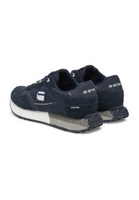 Tumši zili sporta apavi ar ādas un zamša materiālu kombināciju. Tajos ir bieza balta vidējā zole ar plankumainiem akcentiem un teksturētām auklām.