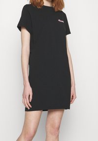 Robe T-shirt en coton noir à manches courtes, avec un petit logo rose sur la poitrine. Coupe droite, texture lisse, longueur au-dessus du genou.