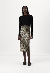 Black fitted long-sleeve top, paired with a leopard-print satin midi skirt in gold and black. Model wears black sandals and sunglasses.
