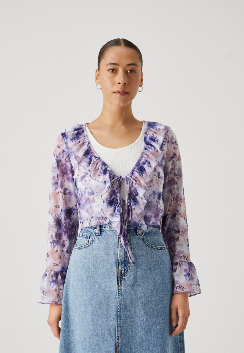 Purple floral sheer blouse with ruffled neckline and sleeves, paired with a light blue denim skirt featuring a high waist and button closure.