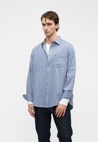 Blauw-wit gestreepte langemouwenshirt, van katoen, met een knoopsluiting aan de voorkant, een enkele borstzak, gelaagd over een wit shirt, met een relaxte pasvorm.