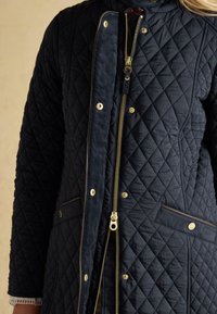 Navy blue quilted jacket with gold zipper and snap buttons, front pockets, and a corduroy inner lining close-up.