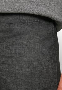 Harmaa, teksturoitu housukangas, jossa sileä pinta. Siinä on hienovarainen, kudottu kuvio ja joustava vyötärönauha.