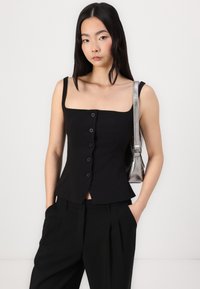 Svart figursydd topp med fyrkantig urringning, fem knappar fram och en peplum nederdel. Matchad med svarta byxor och en metallisk silverhandväska.