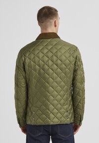 Olivgrüne gesteppte Jacke mit einem Cordkragen, geknöpften Manschetten und seitlichen Druckknöpfen. Hat ein Rautenmuster und eine glatte Textur.
