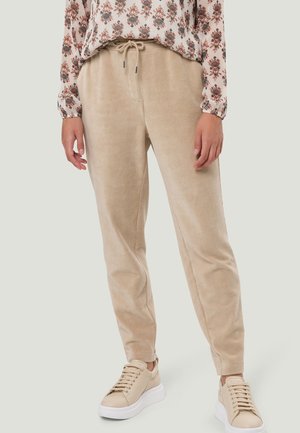 Beige fløjlsbukser med snøre, båret med beige sneakers og en blomsterlangærmet skjorte, vist fra taljen og ned til fødderne.