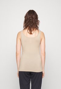Beige ribbed tank top with thin straps, fitted shape, and a seamless back design. Worn with dark loose-fitting pants.