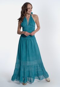 Un lungo abito fluido di colore teal, realizzato in tessuto leggero, con scollo all'americana, volants a strati nella parte inferiore e vita arricciata.