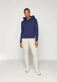 Námořnická modrá mikina s kapucí a stahovací šňůrkou, ribbovaný lem a manžety, spárované se světle béžovými legínami a bílými teniskami. Jednoduchý design a volný střih.