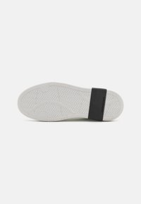 Fehér sneaker talp texturált gumibevonattal és fekete pánttal a hátsó részen, amely cikkcakk mintázattal rendelkezik a tapadás és stabilitás érdekében.