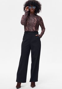 Brązowa bluzka z długim rękawem w wzór wężowy, zestawiona z czarnymi, szerokimi spodniami z wysokim stanem. Dopełnieniem stroju są brązowe botki na obcasie.