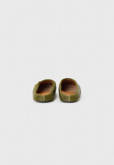 Gröna päls slip-on skor med en slät läderinredning och svart sula. Har mjukt, texturerat material längs kanterna och bakdelen.