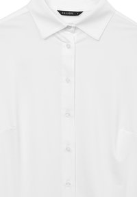 Camicia bianca con colletto a punte e bottoni frontali, con una piccola etichetta nera all'interno del colletto che recita "CALLIOPE S."