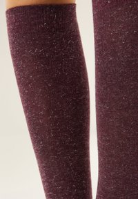 Calzini bordeaux al ginocchio con una texture morbida, caratterizzati da sottili scintillii e un design a maglia fitta. I bordi superiori sono a coste per una migliore vestibilità.