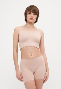 Rebrasti, svijetloružasti crop top i odgovarajuće kratke hlače od rastezljivog materijala. Top ima tanke naramenice i V-izrez; kratke hlače imaju elastičnu traku za struk.